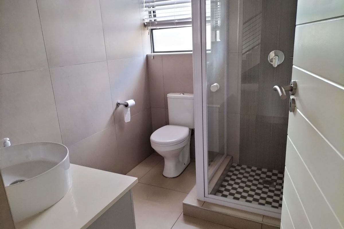 A modern, clean bathroom featuring a vessel sink vanity, a separate shower enclosure with tiled flooring, and neutral wall tiling.