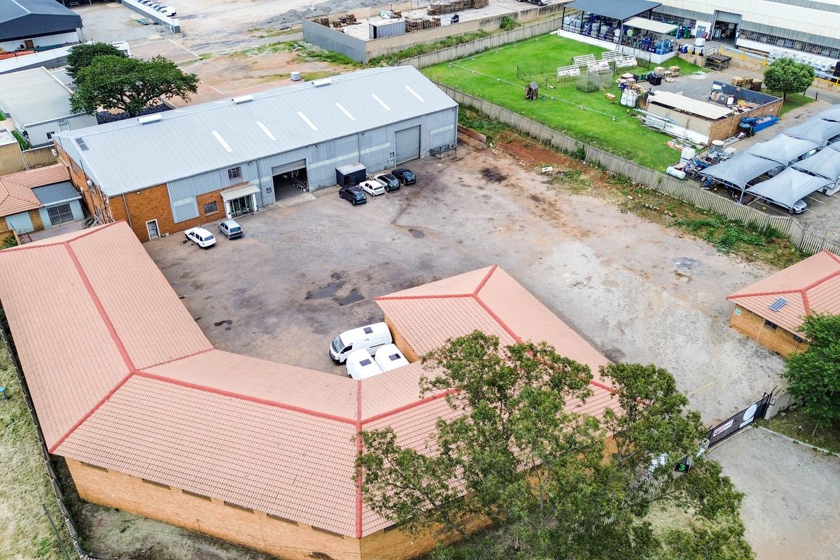 Aerial view of an industrial property featuring a large warehouse, a U-shaped office or workshop building, and a spacious paved yard area.