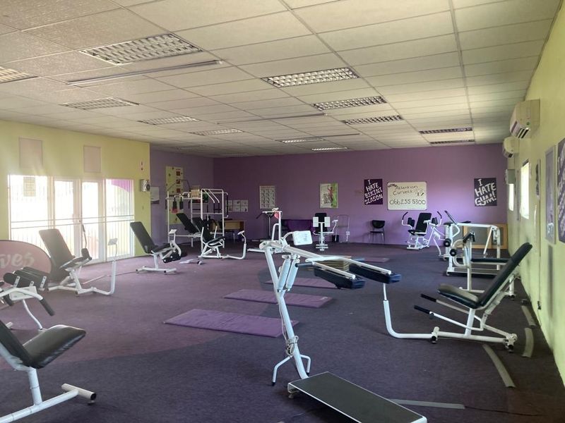 A spacious commercial gym facility featuring a suspended ceiling, recessed lighting, wall-mounted air conditioning, and carpeted flooring.