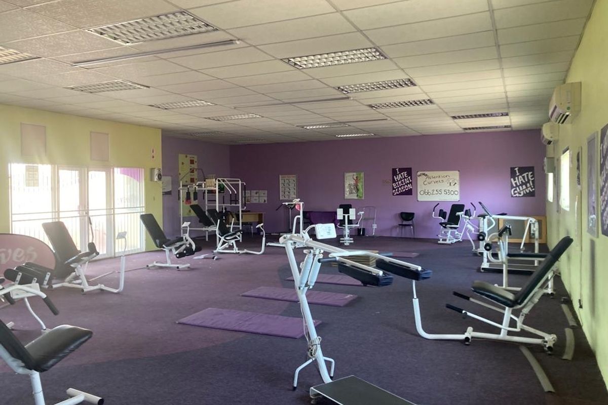 A spacious commercial gym facility featuring a suspended ceiling, recessed lighting, wall-mounted air conditioning, and carpeted flooring.