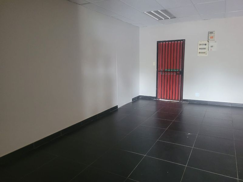 An empty, functional utility space featuring dark tiled flooring, a drop ceiling, and a secure red metal entrance gate.