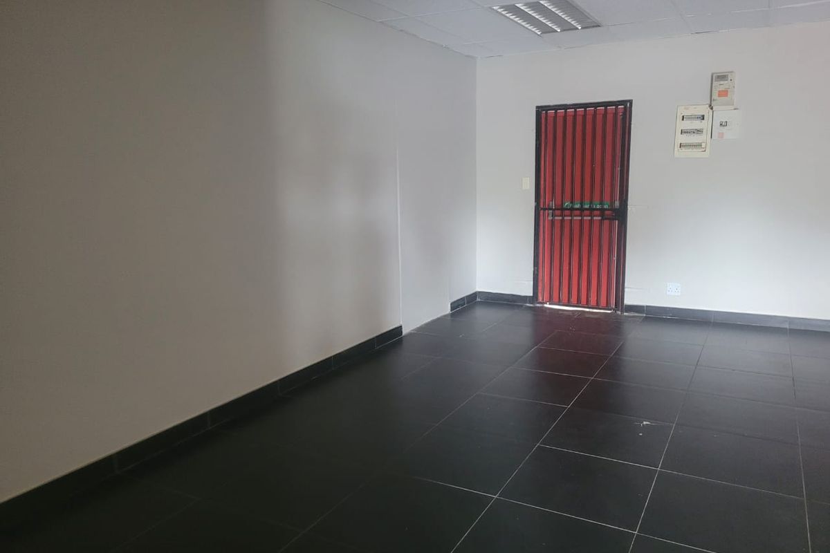 An empty, functional utility space featuring dark tiled flooring, a drop ceiling, and a secure red metal entrance gate.