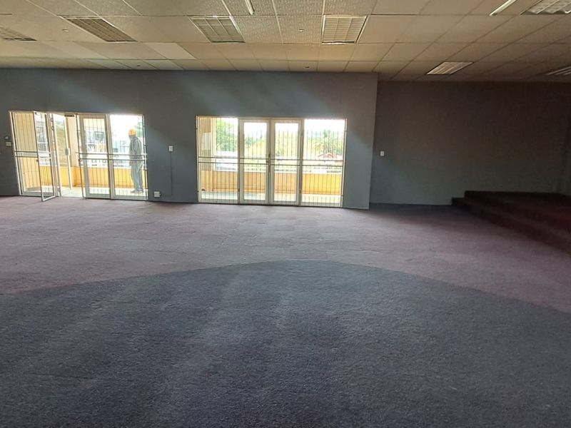 Spacious open-plan retail area featuring a raised platform, suspended ceiling with recessed lighting, and large glass sliding doors with security gates.