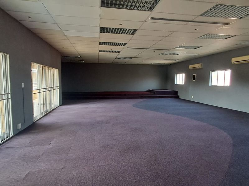 Spacious open-plan retail or commercial area featuring a raised platform stage, suspended ceiling, and split-system air conditioning units.