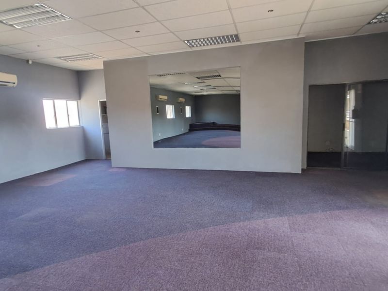 Spacious open-plan retail or office area featuring a suspended ceiling, recessed lighting, wall-mounted air conditioning, and a large feature mirror.