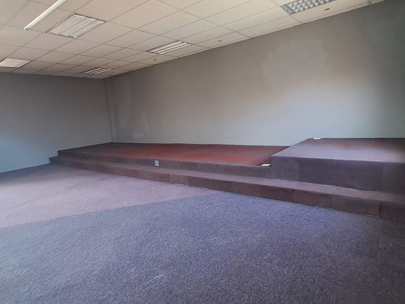 Spacious open-plan retail or commercial area featuring a raised platform stage, suspended ceiling with recessed lighting, and fitted carpeting throughout.