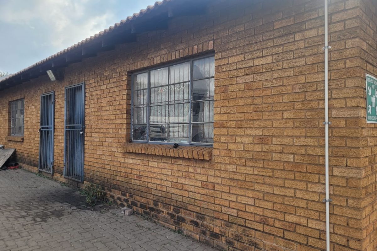 Exterior view of an industrial brick building featuring security-barred windows and doors, with paved access area.