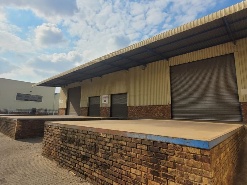 Industrial warehouse exterior featuring multiple loading docks, roller shutter doors, and a protective overhanging roof canopy.