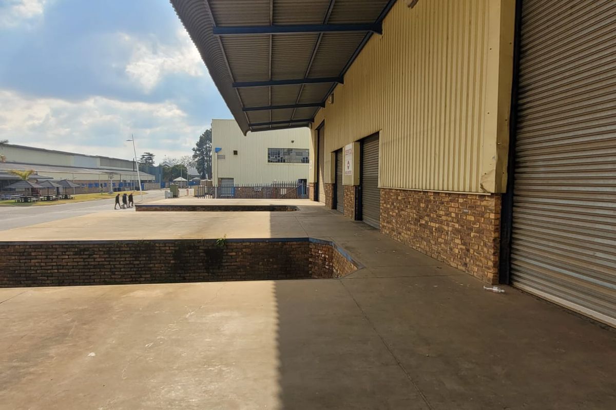 Industrial loading bay area featuring multiple roller shutter doors, a covered canopy, and concrete loading platform access.