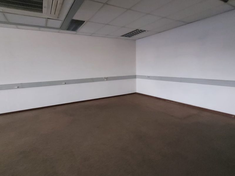 An empty office space featuring a suspended ceiling with recessed lighting, ducted air conditioning, perimeter trunking for cabling, and carpeted flooring.