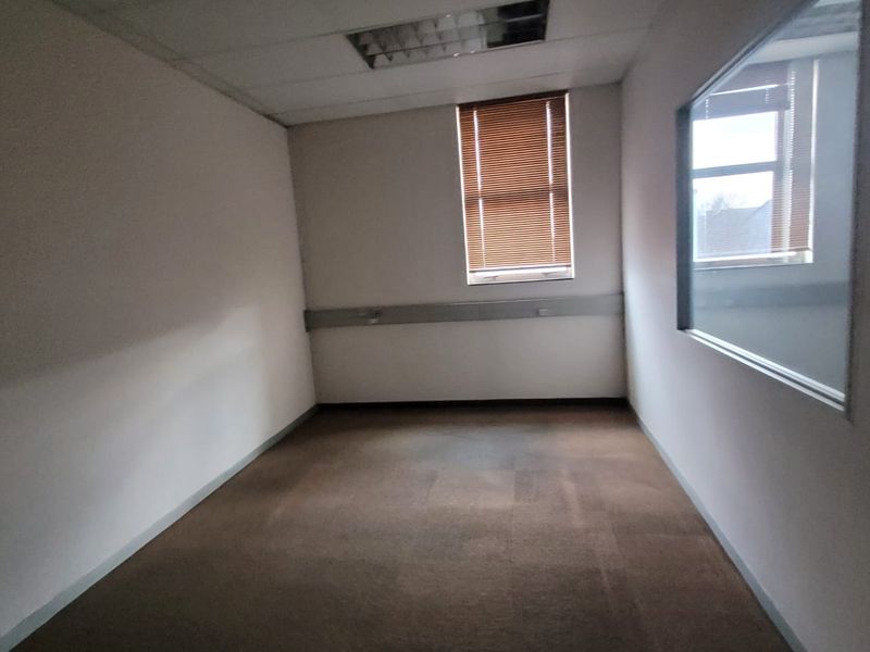 An empty office space featuring a suspended ceiling, recessed lighting, carpet flooring, and an internal glass partition with venetian blinds.