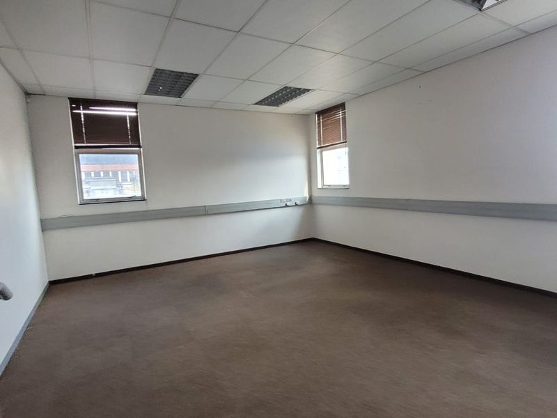 A vacant, open-plan office space featuring a suspended ceiling, recessed lighting, perimeter trunking, and carpeted flooring with large windows providing natural light.