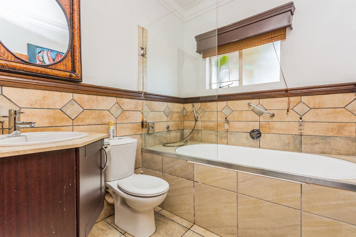 A functional bathroom featuring a built-in bathtub with glass screen, wall-mounted shower mixer, toilet, and a vanity basin with tiled splashback.