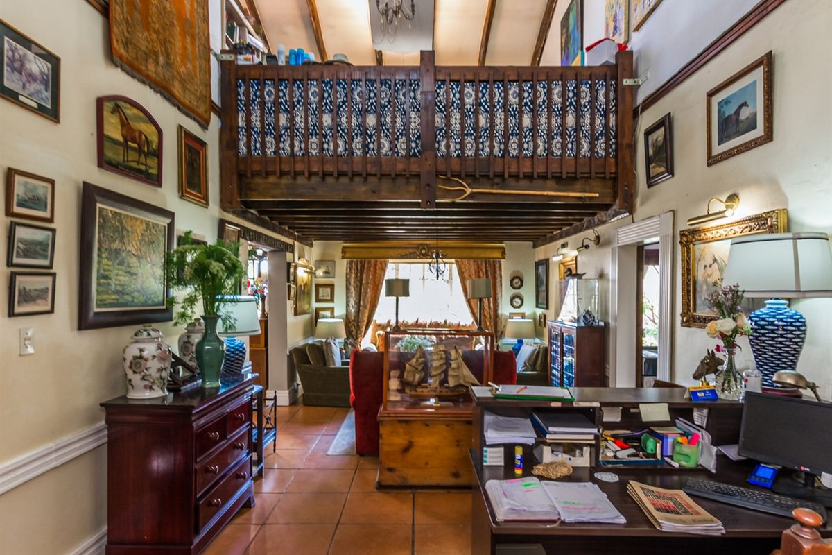 A rustic hotel reception area featuring terracotta floor tiles, exposed timber ceiling beams, and a mezzanine level with a decorative wooden balustrade.