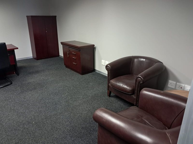 A functional office space featuring neutral wall finishes, dark carpeting, and multiple electrical wall outlets for connectivity.