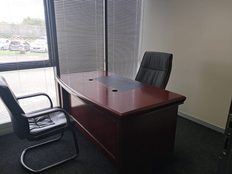 A professional office space featuring large windows with venetian blinds and carpeted flooring, providing a functional work environment.