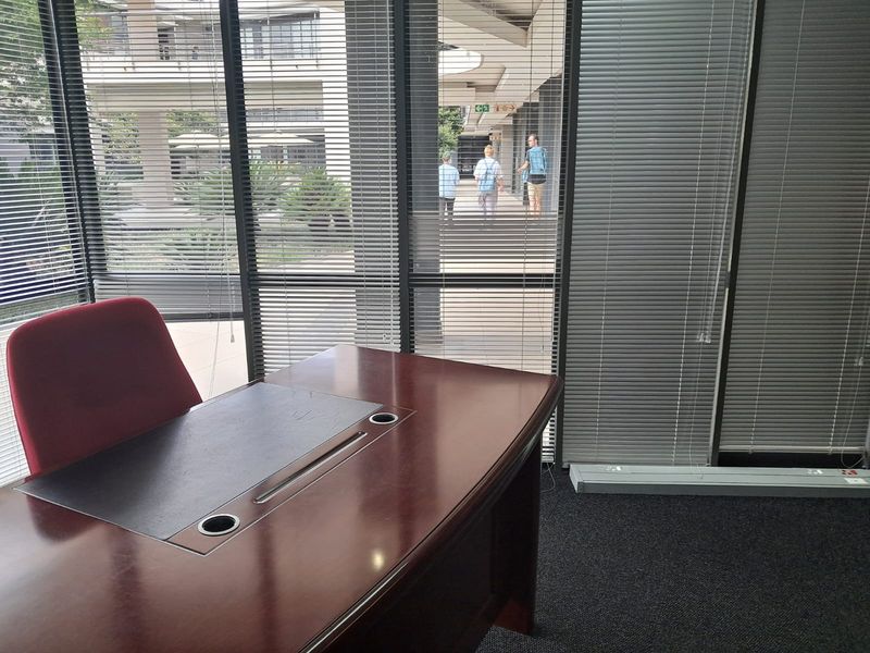 A professional office space featuring large floor-to-ceiling windows with venetian blinds, providing natural light and views of the outdoor courtyard area.
