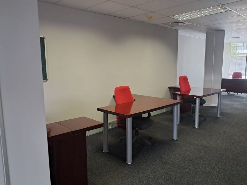 A functional office space featuring carpeted flooring, a suspended ceiling with recessed lighting, and neutral wall finishes.