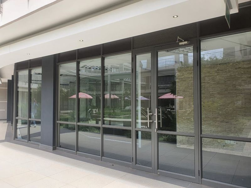 Modern office suite entrance featuring a full-height glass facade, aluminum framing, and a decorative stone feature wall in a professional commercial complex.