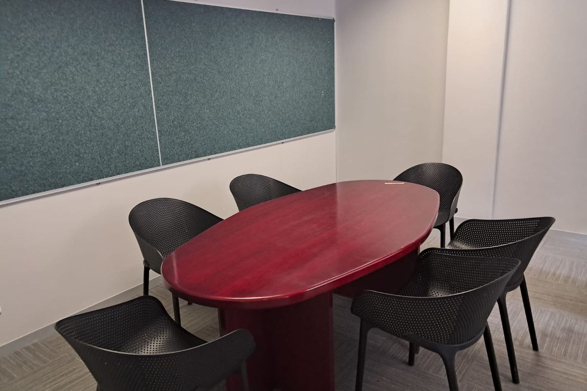 A functional office meeting room featuring a large central table, seating, and a wall-mounted notice board.