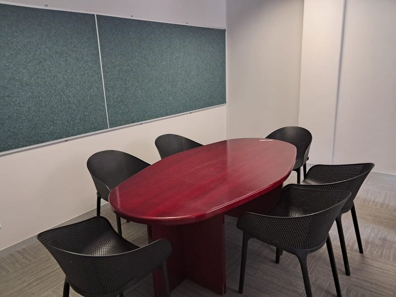 A functional office meeting room featuring a large central table, seating, and a wall-mounted notice board.