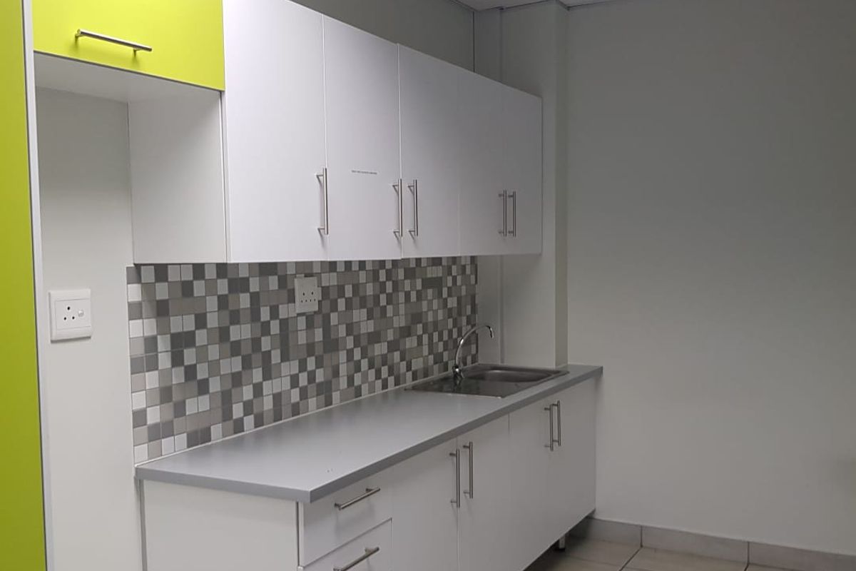 A clean, functional office kitchenette featuring white and lime green cabinetry, a mosaic tile backsplash, and a stainless steel sink.
