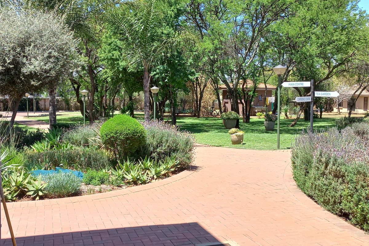 A well-maintained landscaped garden area featuring paved walkways, mature trees, and directional signage leading to various facilities on the office property.