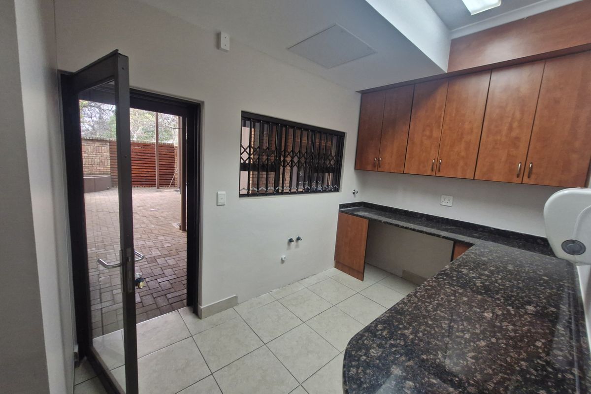 A clean, functional scullery or utility area featuring granite countertops, ample built-in cabinetry, tiled flooring, and direct access to an outdoor paved courtyard.