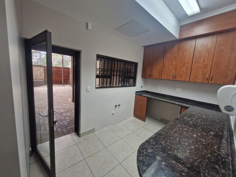 A clean, functional scullery or utility area featuring granite countertops, ample built-in cabinetry, tiled flooring, and direct access to an outdoor paved courtyard.