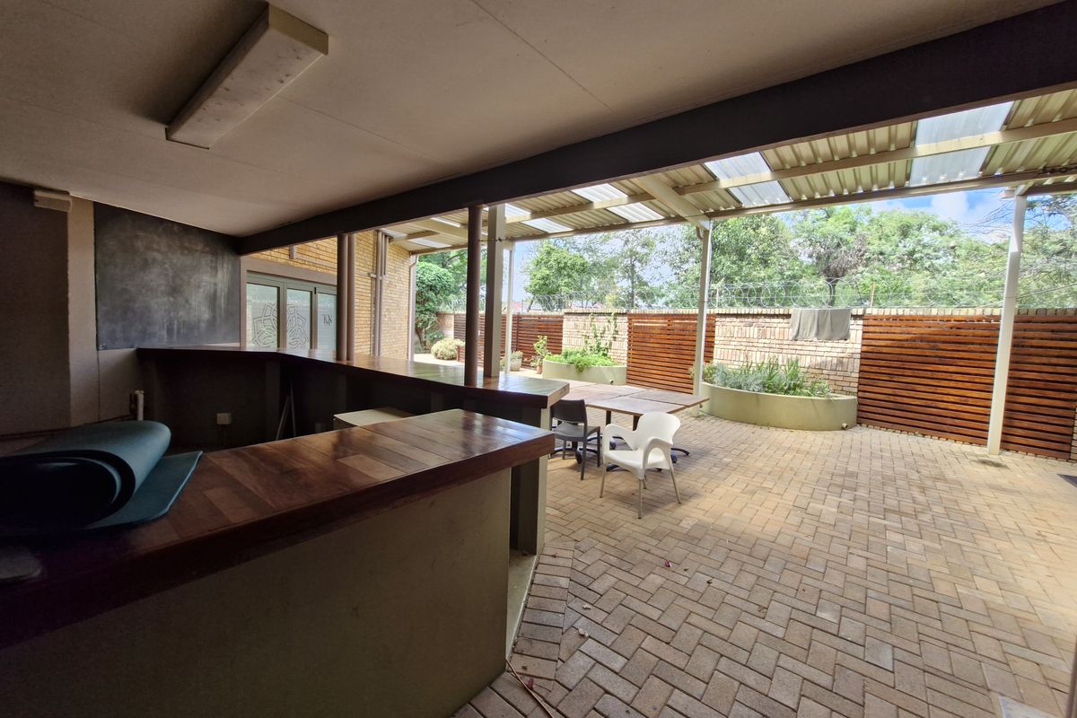 Covered outdoor patio area featuring a built-in bar counter, paved flooring, and integrated garden planters, ideal for office break-out space or social gatherings.