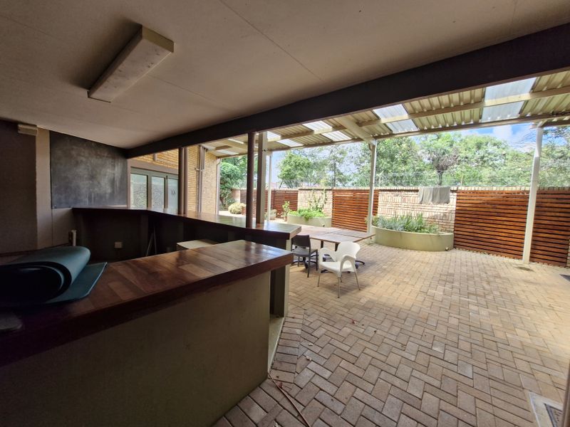 Covered outdoor patio area featuring a built-in bar counter, paved flooring, and integrated garden planters, ideal for office break-out space or social gatherings.