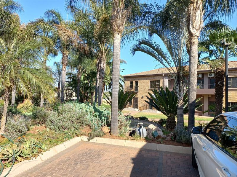 Exterior view of a brick office building featuring a well-maintained landscaped garden with mature palm trees and a paved driveway.