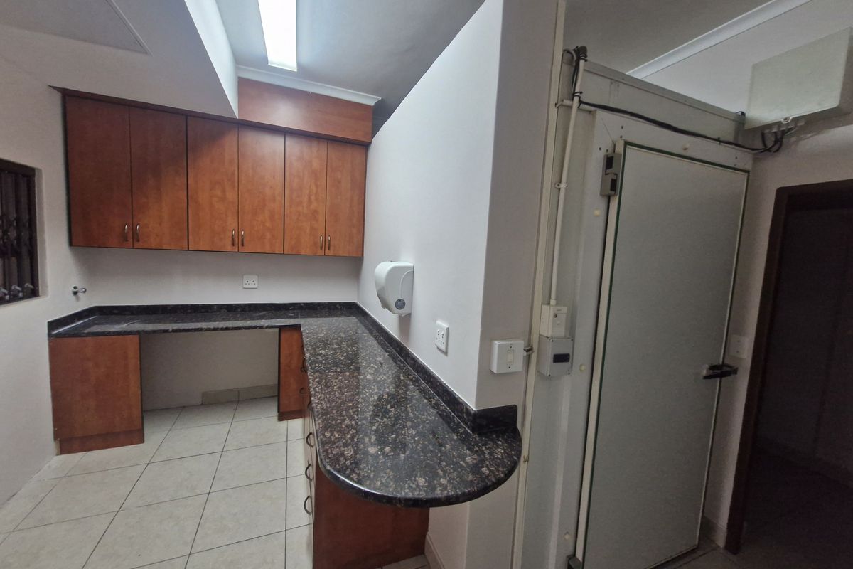 A functional office kitchen area featuring laminate cabinetry, granite countertops, and a dedicated walk-in cold storage unit.