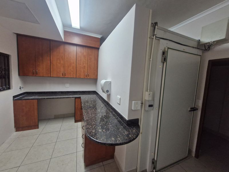 A functional office kitchen area featuring laminate cabinetry, granite countertops, and a dedicated walk-in cold storage unit.