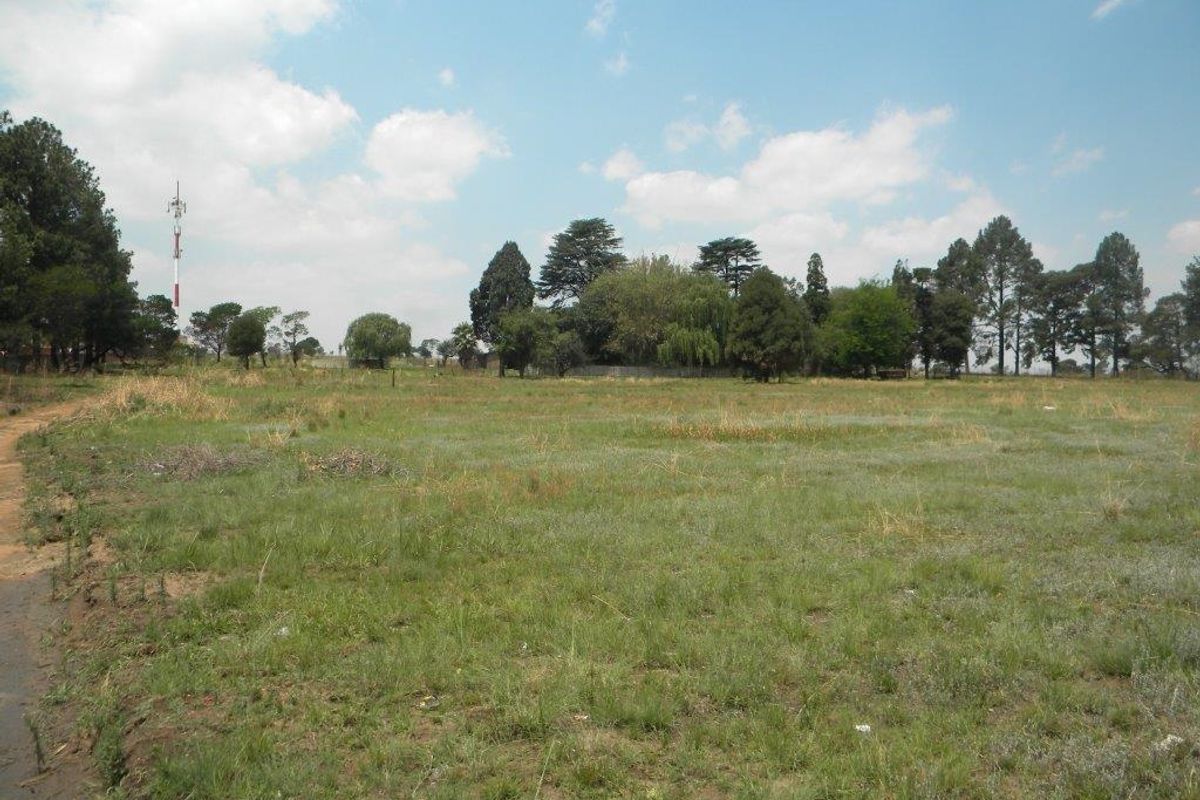 A wide-angle view of a vacant residential plot featuring open grassland and mature trees in the background.