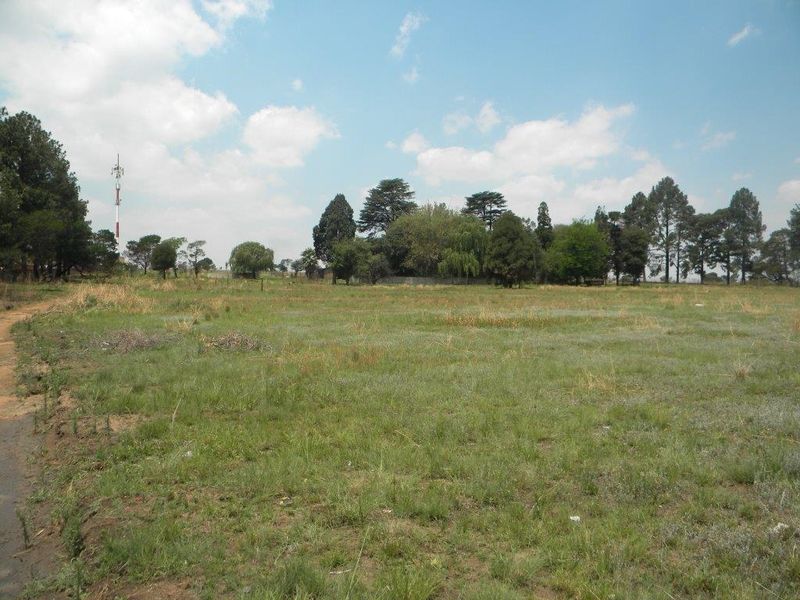 A wide-angle view of a vacant residential plot featuring open grassland and mature trees in the background.