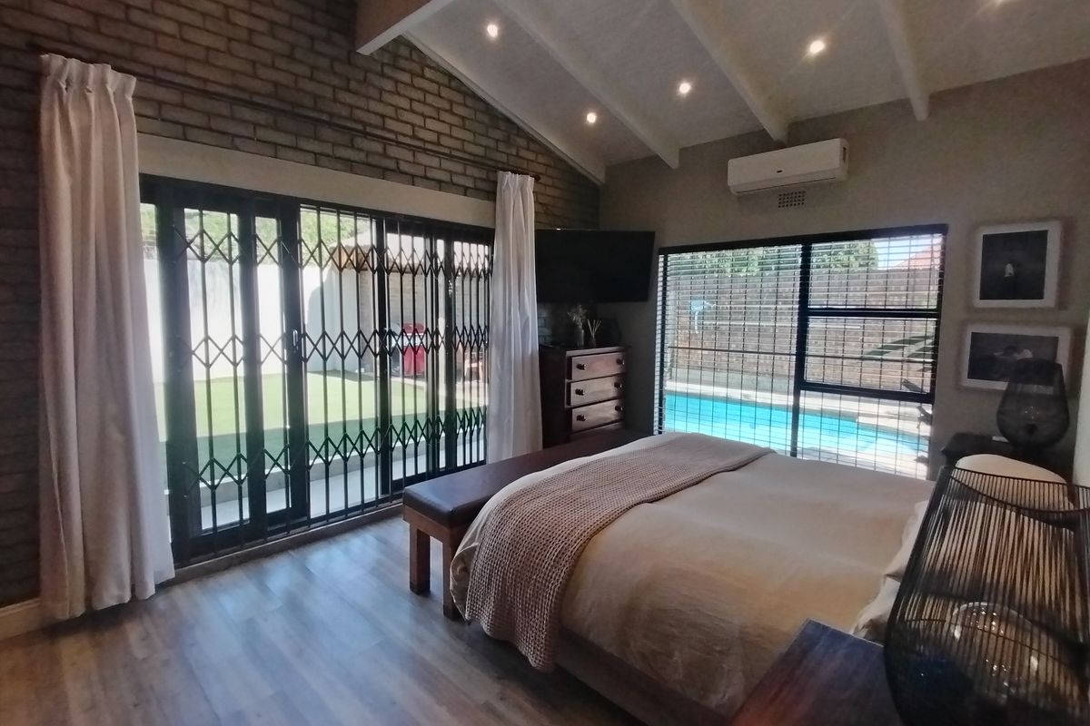 Spacious bedroom featuring exposed brick walls, vaulted ceilings with recessed lighting, laminate flooring, and direct access to the pool area through sliding glass doors.