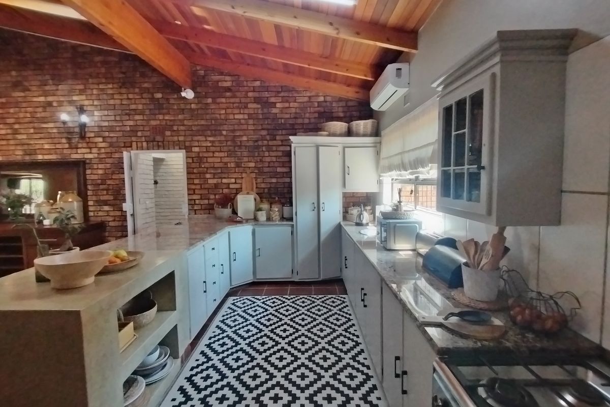 Spacious kitchen featuring exposed timber beams, brick feature wall, stone countertops, and ample built-in cabinetry with a gas cooktop.