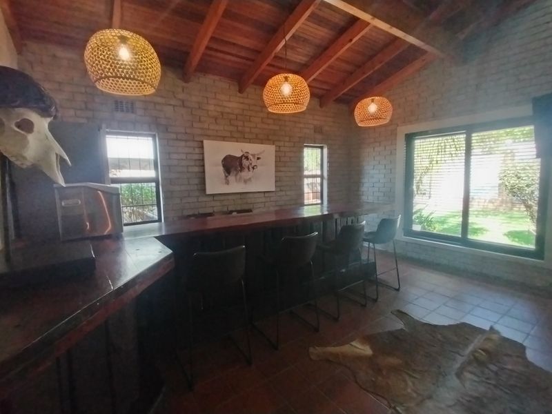 A rustic bar area featuring exposed brick walls, a timber beam ceiling, tiled floors, and a built-in bar counter with direct garden access.