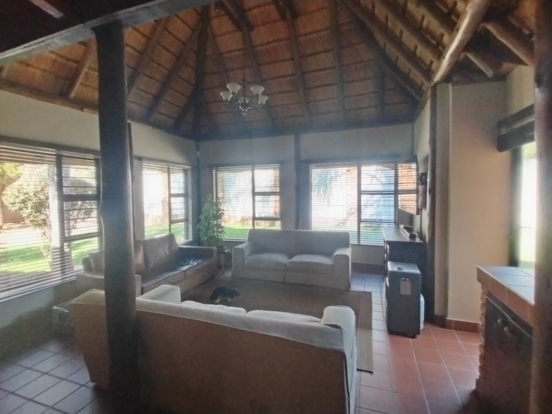 Spacious living area featuring a high thatched ceiling, exposed timber support poles, and terracotta floor tiles with abundant natural light from large windows.