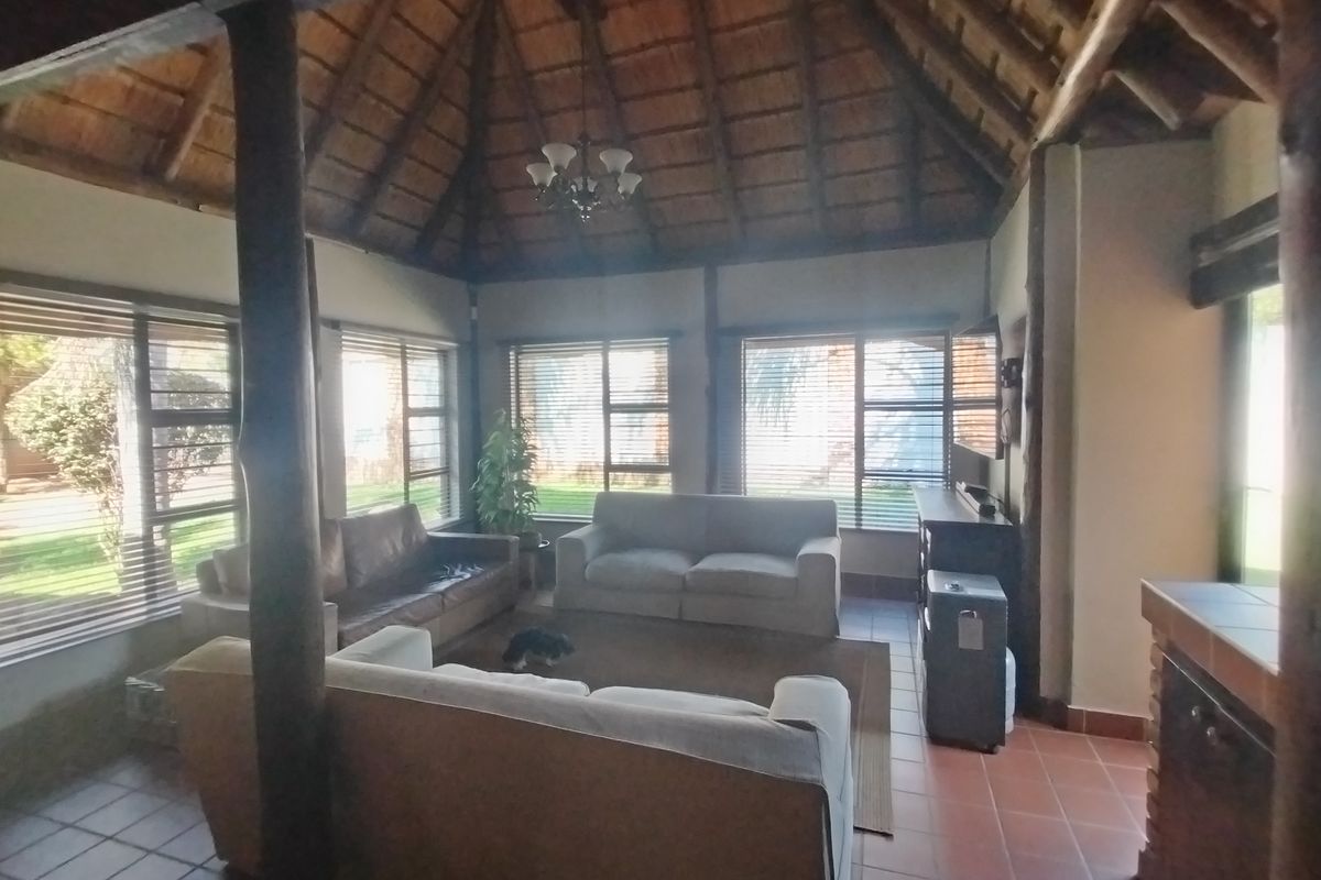 Spacious living area featuring a high thatched ceiling, exposed timber support poles, and terracotta floor tiles with abundant natural light from large windows.