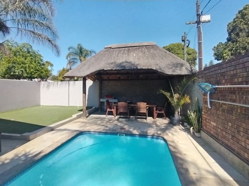 Outdoor entertainment area featuring a swimming pool and a covered thatched lapa with a built-in braai, set within a private walled garden.