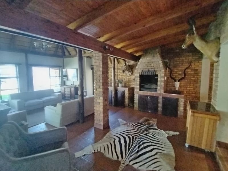 Spacious open-plan living area featuring exposed timber beam ceilings, a prominent brick fireplace, and tiled flooring throughout.