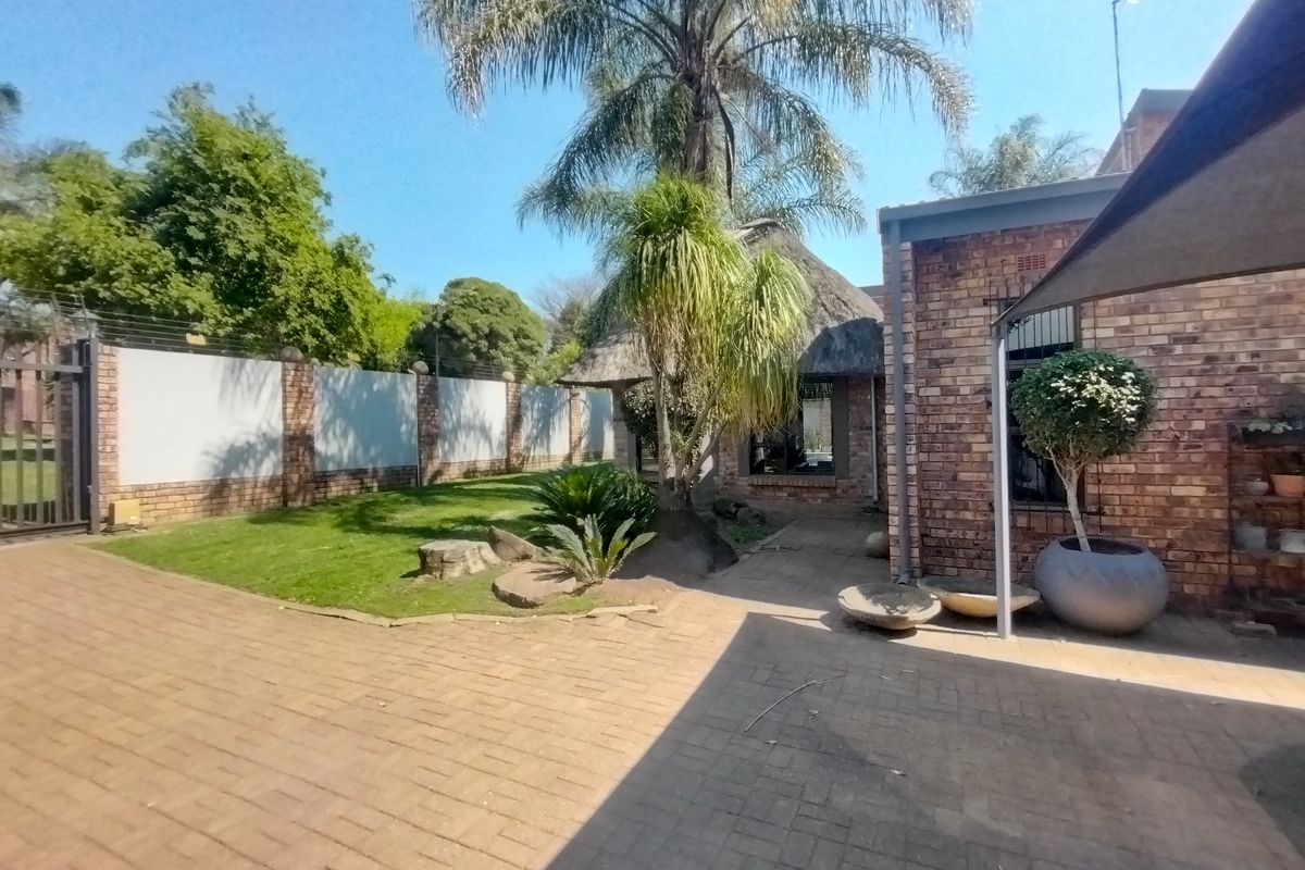 A rear garden area featuring brick paving, a thatched roof structure, and a secure perimeter wall with electric fencing.