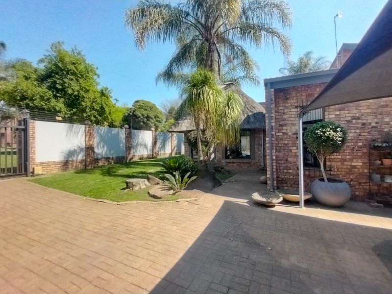 A rear garden area featuring brick paving, a thatched roof structure, and a secure perimeter wall with electric fencing.