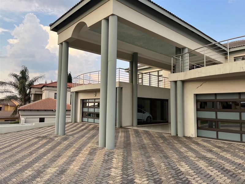 Front elevation featuring a paved driveway, covered entrance with prominent structural columns, and multiple garage doors with a balcony above.