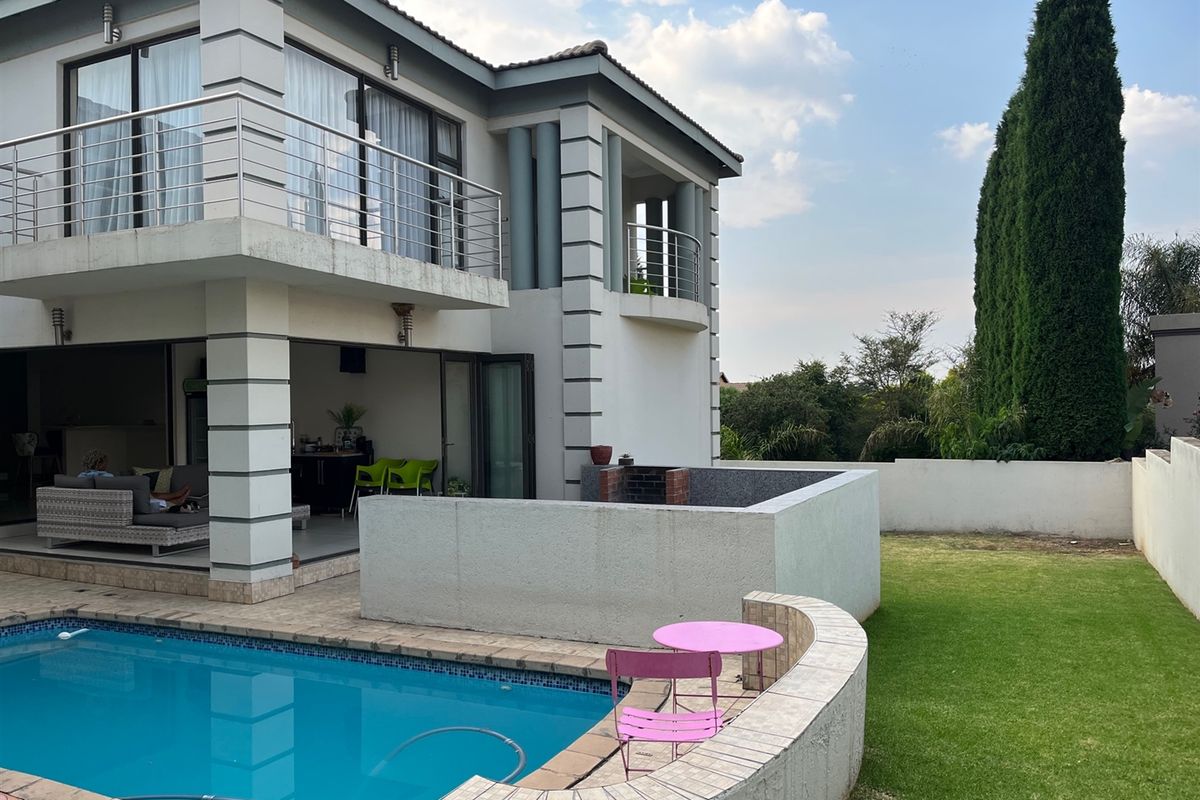 Rear view of a double-story house featuring a swimming pool, a built-in braai area, and an upper-level balcony overlooking the garden.