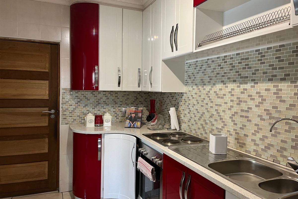 A compact kitchen featuring high-gloss red and white cabinetry, a mosaic tile backsplash, stone countertops, and integrated electric cooking appliances.