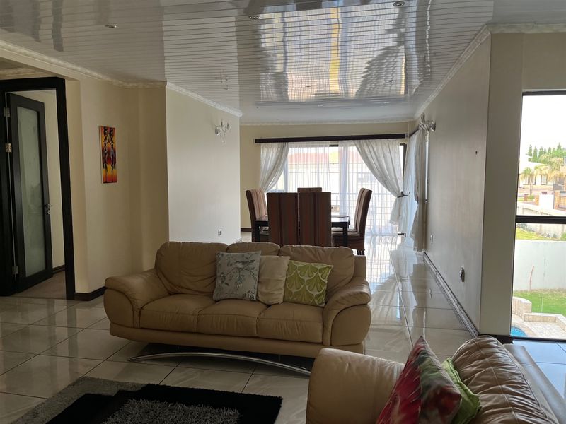 Spacious open-plan living and dining area featuring glossy ceiling finishes, large format floor tiles, and sliding glass doors providing natural light and garden access.