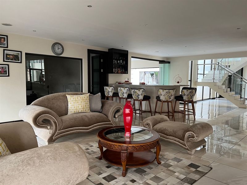 Spacious open-plan living area featuring a built-in bar, polished tiled flooring, and a modern staircase with a glass balustrade.
